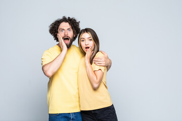 Happy excited couple standing with hands at their face and looking at camera over gray background