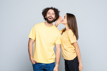 Fototapeta premium Excited couple telling secrets to each other standing isolated over gray background,