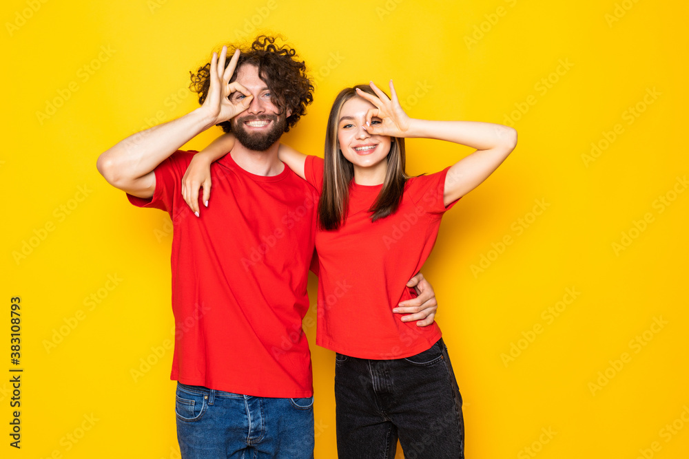 Wall mural excited beautiful couple wearing white t-shirts standing isolated over yellow background,