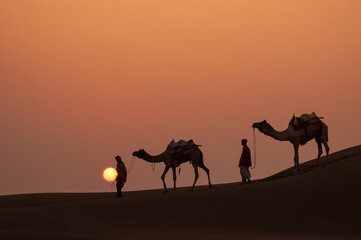Man and a camel walking across sand dunes in Jaisalmer, Rajasthan, India.