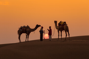 Fototapeta na wymiar Man and a camel walking across sand dunes in Jaisalmer, Rajasthan, India.