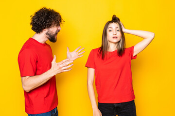 Portrait couple man and woman screaming at each other during fight over yellow background