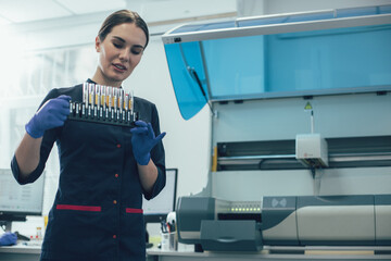 Attentive woman in medical uniform looking at the test tubes