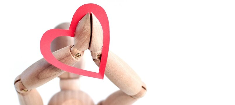 Red paper heart on the hands of a wooden mannequin on white background. Trendy minimal concept of Valentine's day, love, real feeling. Banner.