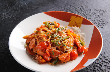 Japanese cuisine. Noodles with fried tomatoes, vegetables and herbs on a bright plate on a black background. Background image, copy space