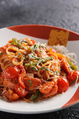 Japanese cuisine. Noodles with fried tomatoes, vegetables and herbs on a bright plate on a black background. Background image, copy space