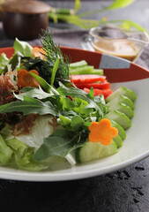 Japanese cuisine. Raw sliced vegetables: cucumber, pepper, carrot and broccoli. Arugula, lettuce, dill and sauce on a plate on a black table with chopsticks. Background image, copy space