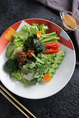 Japanese cuisine. Raw sliced vegetables: cucumber, pepper, carrot and broccoli. Arugula, lettuce, dill and sauce on a plate on a black table with chopsticks. Background image, copy space, flatlay