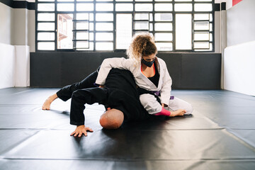 Man and woman training martial arts and judo with kimonos on the gym floor mat with a face mask because of the covid 19 coronavirus pandemic