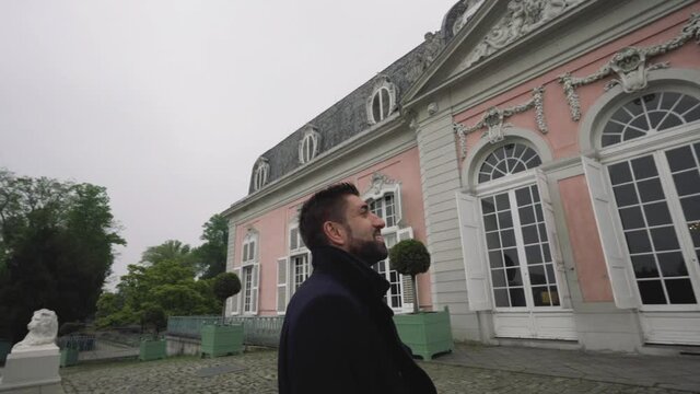Man stands in front of the Benrath Palace and looks enthusiastically at the pink old facade. Dusseldorf, Germany