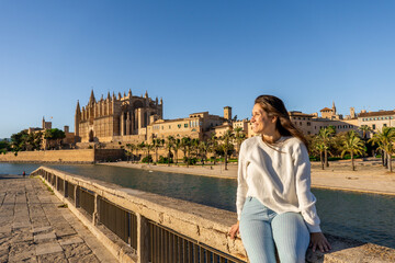 Young light-skinned girl taking a picture of the cathedral of Palma de Mallorca with her phone on her holidays. © MinekPSC