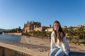 Fototapeta na wymiar Young light-skinned girl taking a picture of the cathedral of Palma de Mallorca with her phone on her holidays.