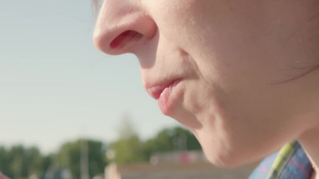 Closeup side view of faceless young woman eating muffin using fork against the background of blurred public park.