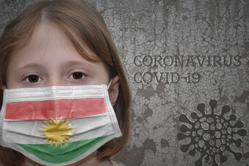Little girl in medical mask with flag of kurdistan stands near the old vintage wall with text coronavirus, covid, and virus picture. Stop virus concept