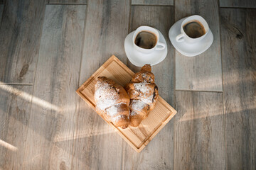 Fresh pastries croissants with chocolate on a wooden board and two cups of black coffee. Romantic breakfast