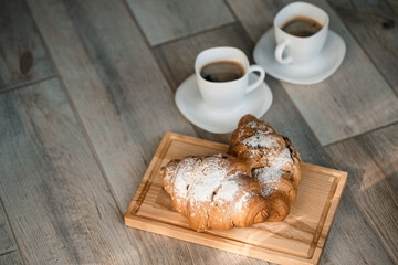 Fresh pastries croissants with chocolate on a wooden board and two cups of black coffee. Romantic breakfast