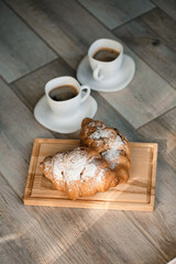 Fresh pastries croissants with chocolate on a wooden board and two cups of black coffee. Romantic breakfast
