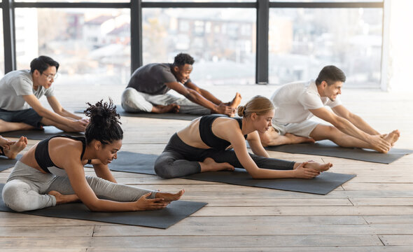Diverse sporty men and women doing stretching exercises during group yoga lesson