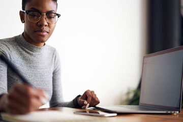 Crop ethnic female manager writing in notebook at office