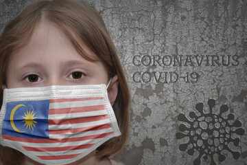 Little girl in medical mask with flag of malaysia stands near the old vintage wall with text coronavirus, covid, and virus picture. Stop virus concept