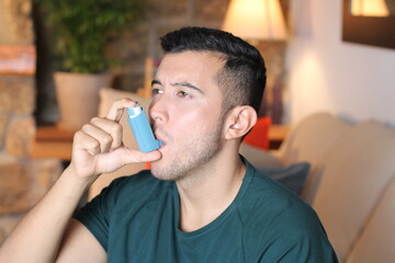 Young ethnic man using asthma inhaler at home
