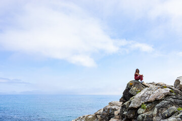 general shot of the Galician coast with a woman perched on some rocks observing the horizon