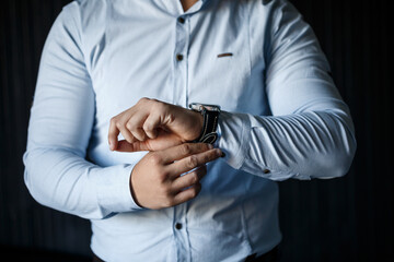 A man elegant businessman buttons a watch on his hand he is dressed in a white dress shirt