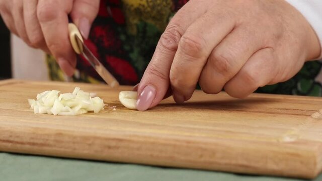 cut garlic with knife above a wooden cutting board, side view