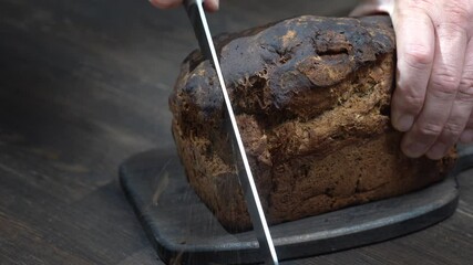 Cutting two slices of brown bread on wooden board. Cut the whole grain bread with a knife. Close up of dark bread, healthy lifestyle.