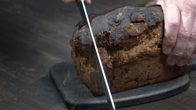 Cutting two slices of brown bread on wooden board. Cut the whole grain bread with a knife. Close up of dark bread, healthy lifestyle.