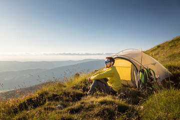 seated man in front of a tente in mountains with panoramic view