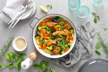 Chicken drumsticks roasted with vegetables in cast iron pan on kitchen table, top down view