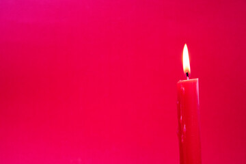 One burning red candle on a red background - Advent, birthday or christmas scene