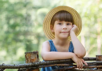 Poster Portret van schattig klein meisje in het bos. Schattige peuter met een hoed leunt op een houten hek © Albert Ziganshin
