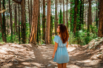 Beautiful young woman with long hair in a dress walking alone in a pine forest