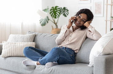 Fototapeta premium Mobile Communication. Cheerful african woman talking on cellphone with friends at home