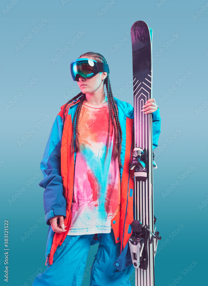 Wall mural cool sporty young girl skier in stylish winter sportswear and snowboarding goggles with ski on blue 