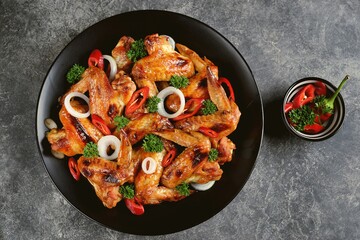 Delicious grilled chicken wings with chili pepper, onion and parsley on concrete background. Top view. 