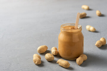 Homemade peanut butter in a glass jar on a concrete surface.
