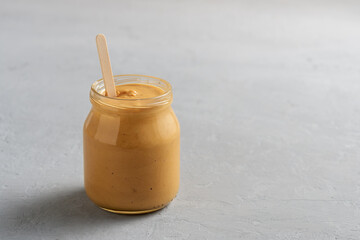 Homemade peanut butter in a glass jar on a concrete surface.