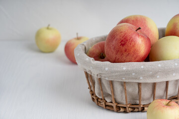 Group of organic tasty red and yellow apples in wicker basket on simple white wooden background at kitchen showing healthy lifestyle and vegetarian dietary eating. Image with copy space, horizontal