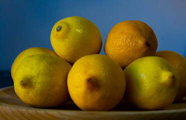 Fototapeta na wymiar Lateral view of a small mountain of lemons on a wooden plate with a bluish background