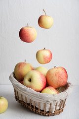 Wicker basket full of organic apples with ripe juicy fruits falling or levitating on simple white wooden background at kitchen table showing healthy lifestyle and vegetarian dietary eating. Vertical