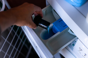 Top view, you can see how a person is putting a blue detergent product inside a washing machine to wash clothes