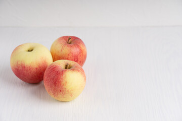 Three organic tasty red and yellow apples on simple white wooden background at kitchen showing healthy lifestyle and vegetarian dietary eating. Image with copy space, horizontal orientation