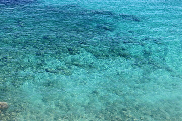 Azure water texture, transparent sea surface with a rocky bottom. Aerial view, natural blue background