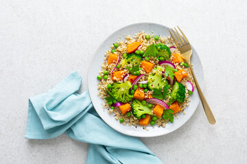 Vegetarian quinoa and broccoli warm salad with baked butternut squash or pumpkin, green peas and fresh red onion, top down view