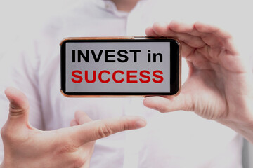Businessman holding a phone with a message text invest in success written on it. Business concept