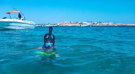 man in a full face snorkeling mask floats on the sea.
