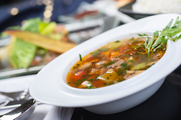 Traditional vegetable soup broth in a white plate on a table in a restaurant.
